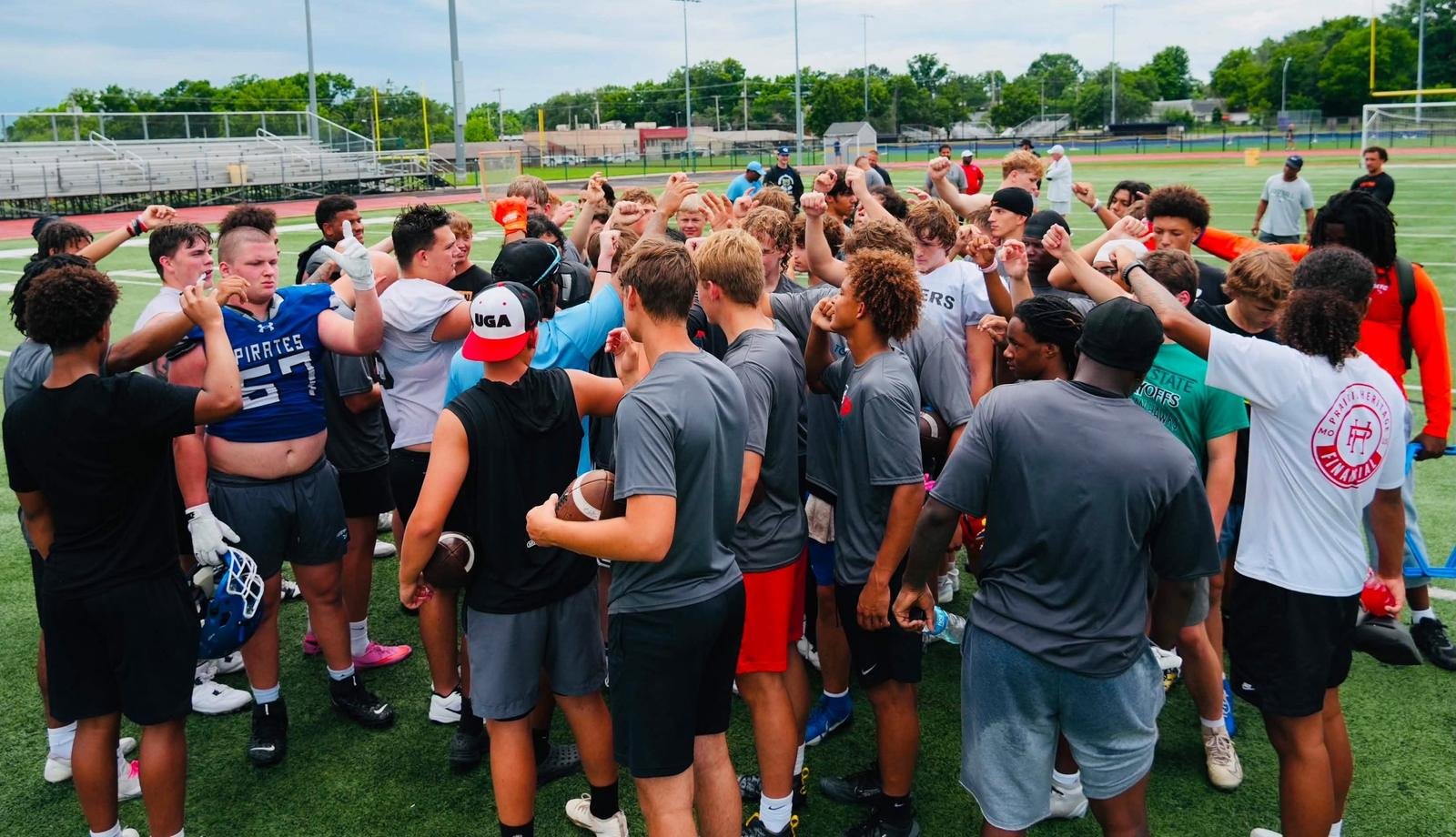 Dozens of high school athletes with fists raised in a camp huddle